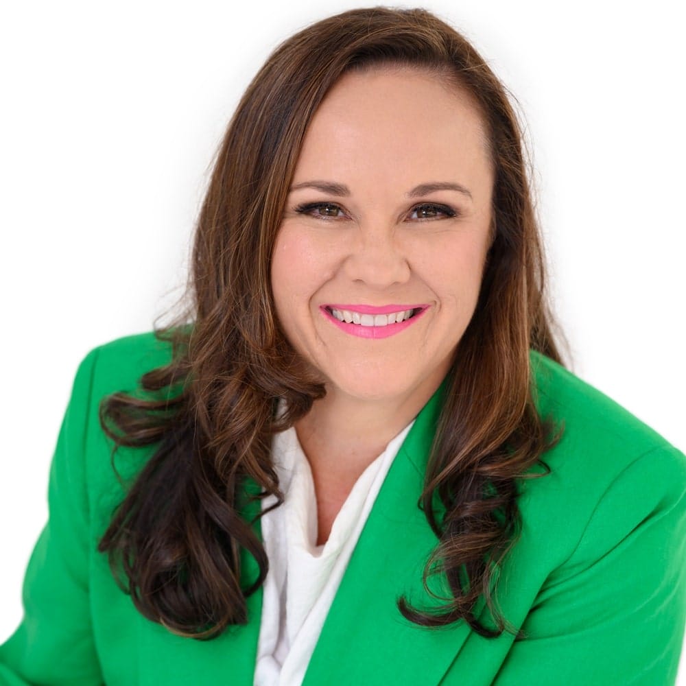 Natasha-Doherty-green-suit-white-backdrop A cropped headshot of Natasha Doherty wearing a green suit, with only the top half of her head and shoulders visible against a plain white backdrop.