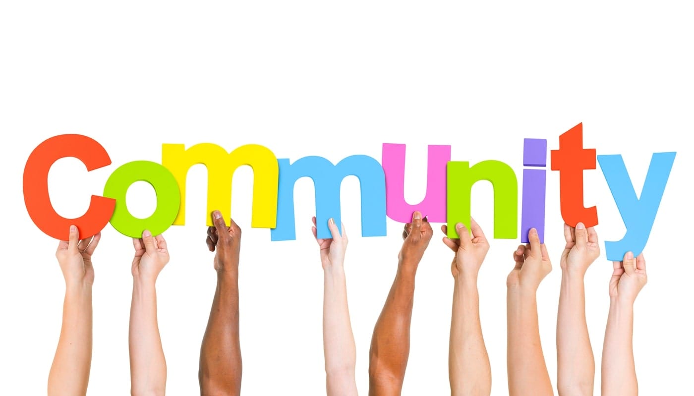hands-holding-community-sign Hands of people from various racial backgrounds holding a sign that says "community," representing unity and shared purpose.